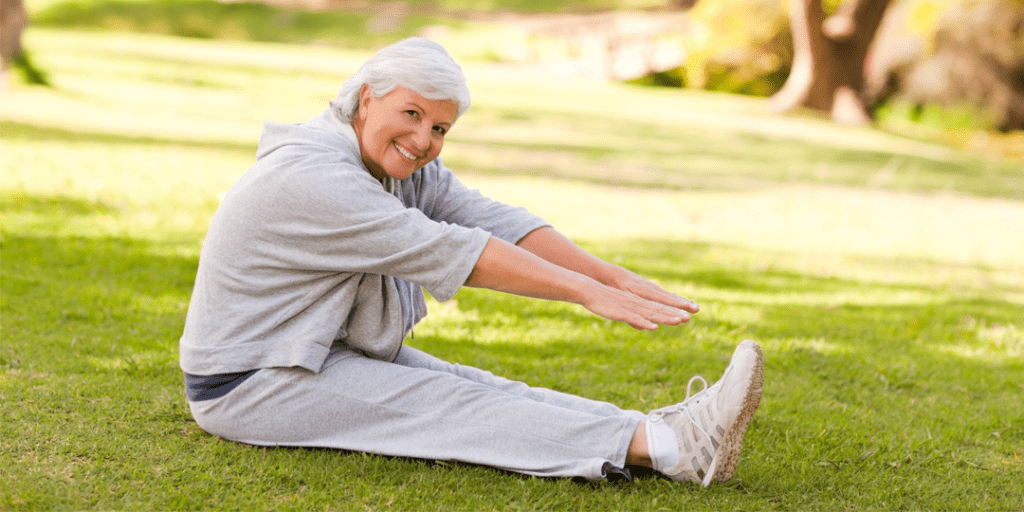 Senior woman sitting outside under a tree doing leg stretches