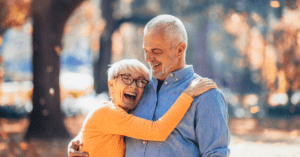 Happy older couple embrace outdoors under trees with autumn leaves