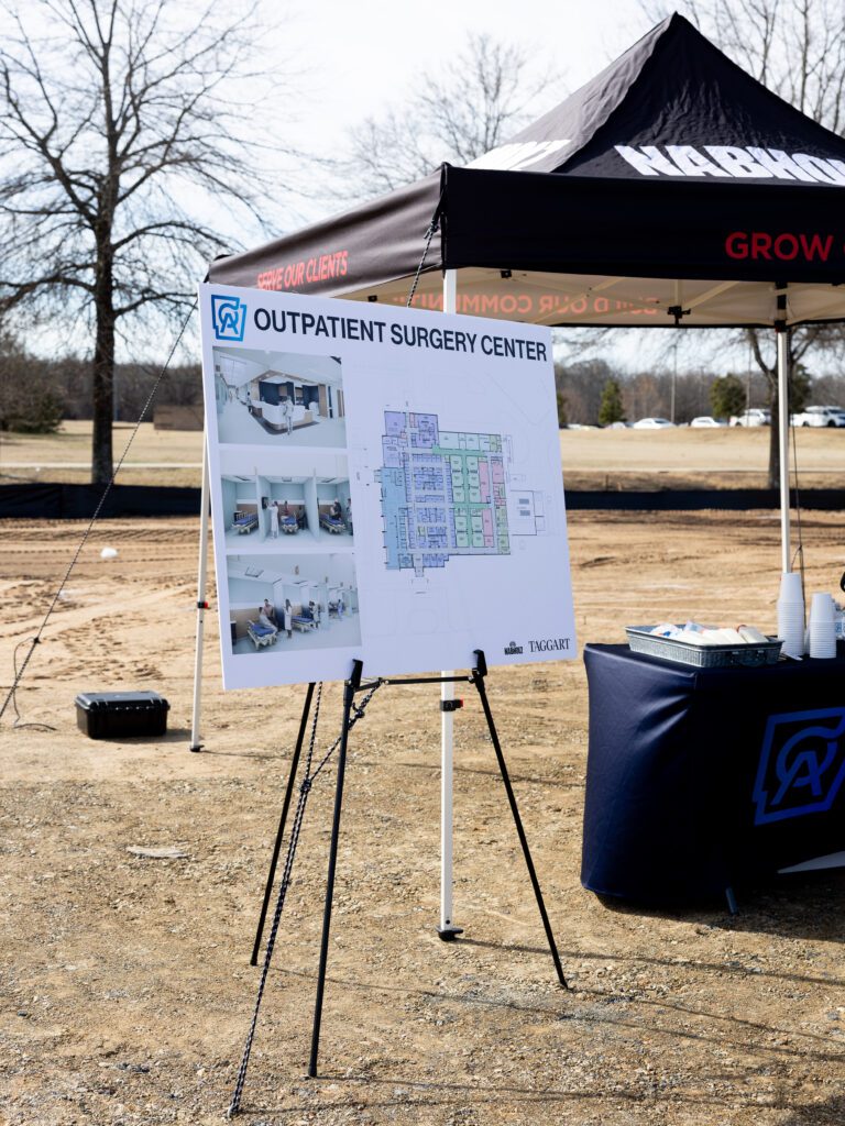 A display board on a tripod easel showing a detailed floor plan and three interior design renderings of the new OrthoArkansas Outpatient Surgery Center.