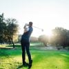 Male golf player teeing off golf ball from tee box to beautiful sunset